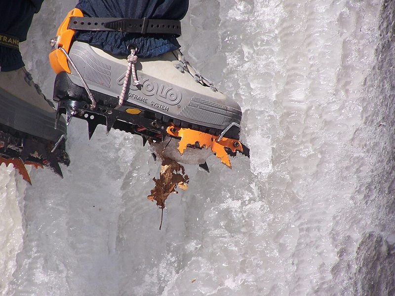 A mountaineering boot fitted with orange crampons on a frozen ice wall