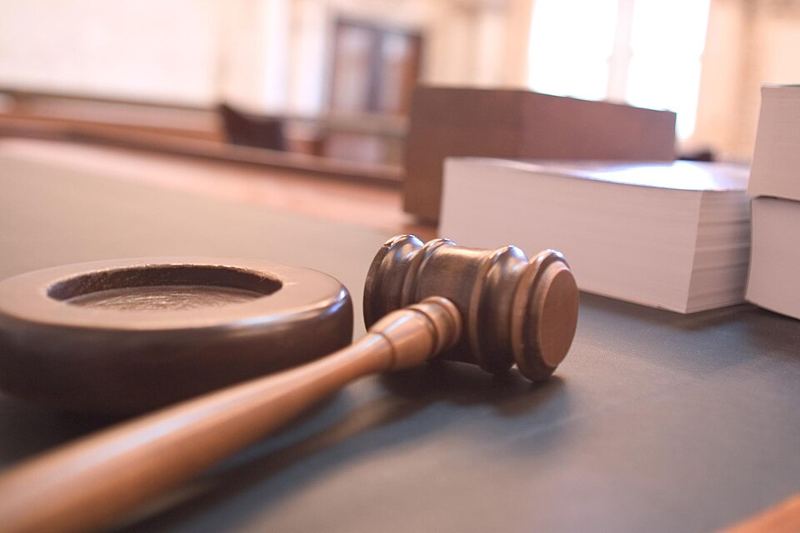 A wooden judge's gavel and sound block on a courtroom bench beside stacks of documents