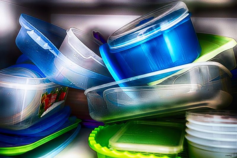 A pile of reusable plastic food storage containers with blue, clear, and green lids