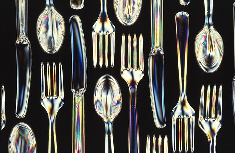 Clear knives, forks, and spoons made from biodegradable starch-polyester plastic on a black background