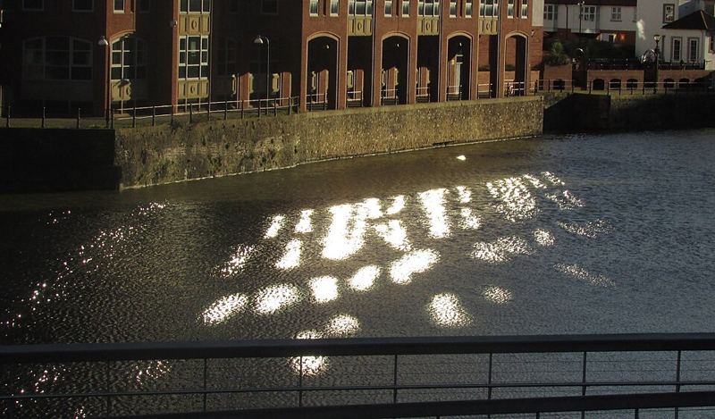 Sunlight reflecting on the water of the Floating Harbour in Bristol, England, beside red-brick buildings