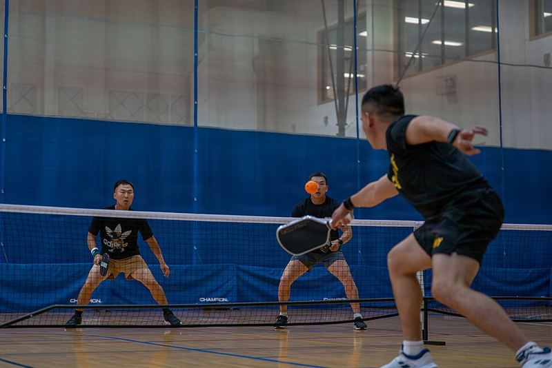 Doubles pickleball players at the net waiting to return a serve in an indoor gym