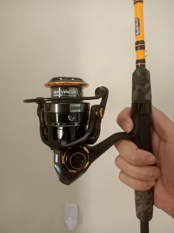 Hand holding a fishing rod with a black and orange spinning reel