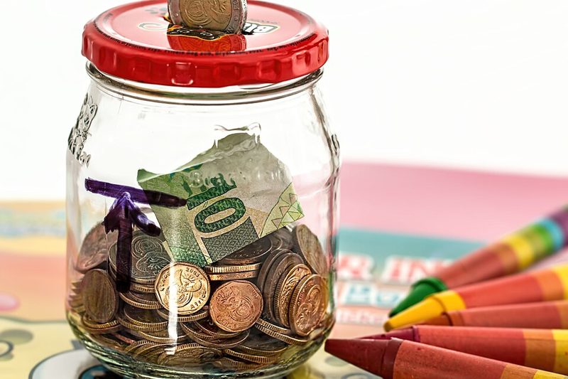 Glass savings jar holding coins and a banknote