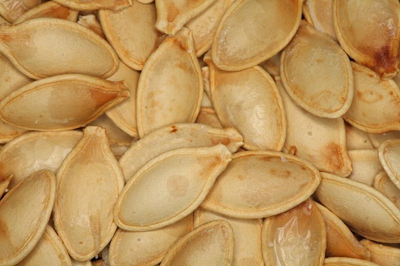 Close-up of a pile of cream-colored, oval roasted pumpkin seeds still in their shells