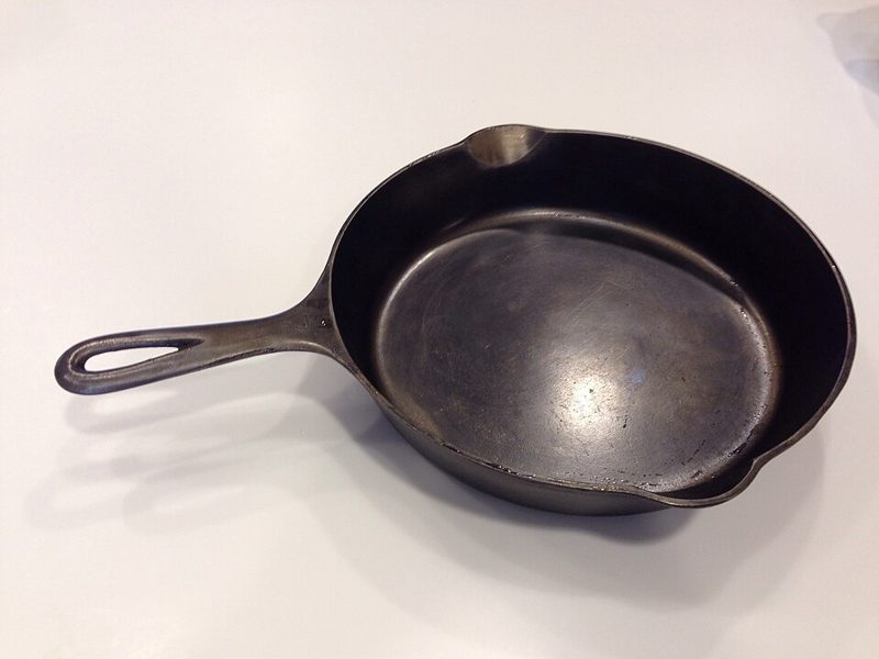 Seasoned black cast iron skillet with a pour spout resting on a white countertop