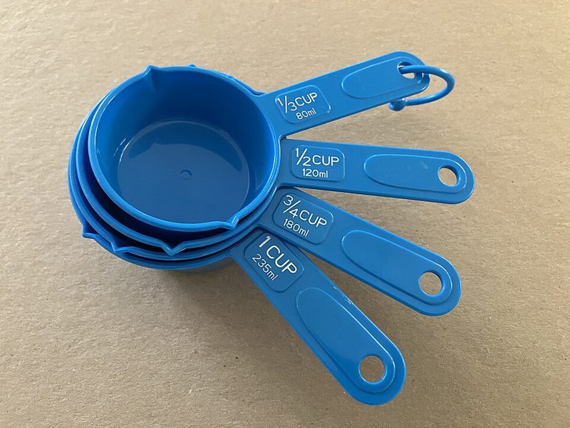 Set of US measuring cups marked in cups and milliliters, used with a cooking conversion chart