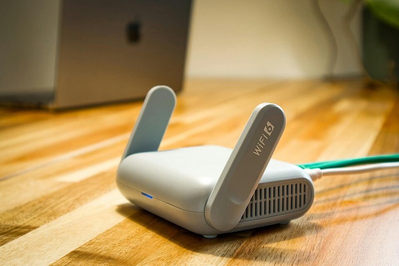 A small white Wi-Fi 6 travel router with two antennas on a wooden desk