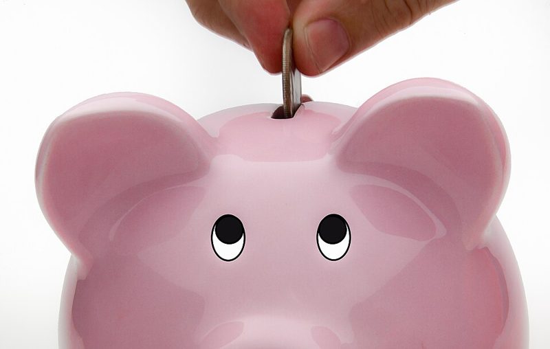A hand dropping a coin into a piggy bank labeled as a savings account
