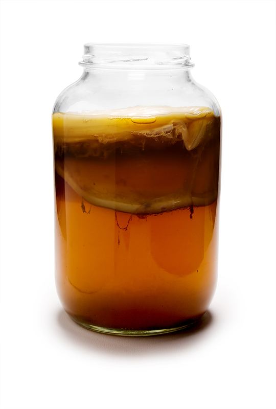 Glass jar of amber kombucha with a SCOBY culture floating near the top
