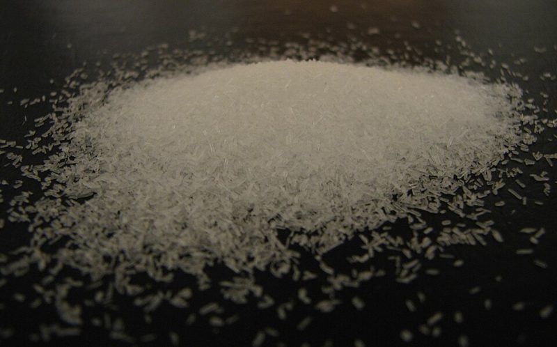 A small pile of white monosodium glutamate (MSG) crystals on a dark surface