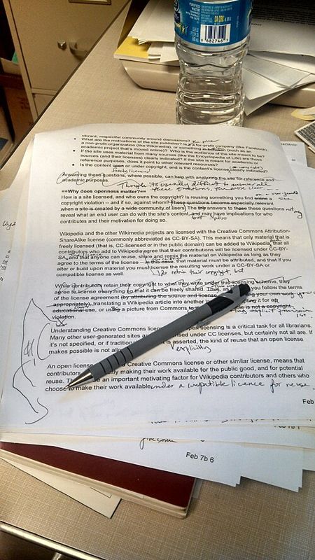 Printed manuscript page marked up with handwritten edits, with a pen resting on it