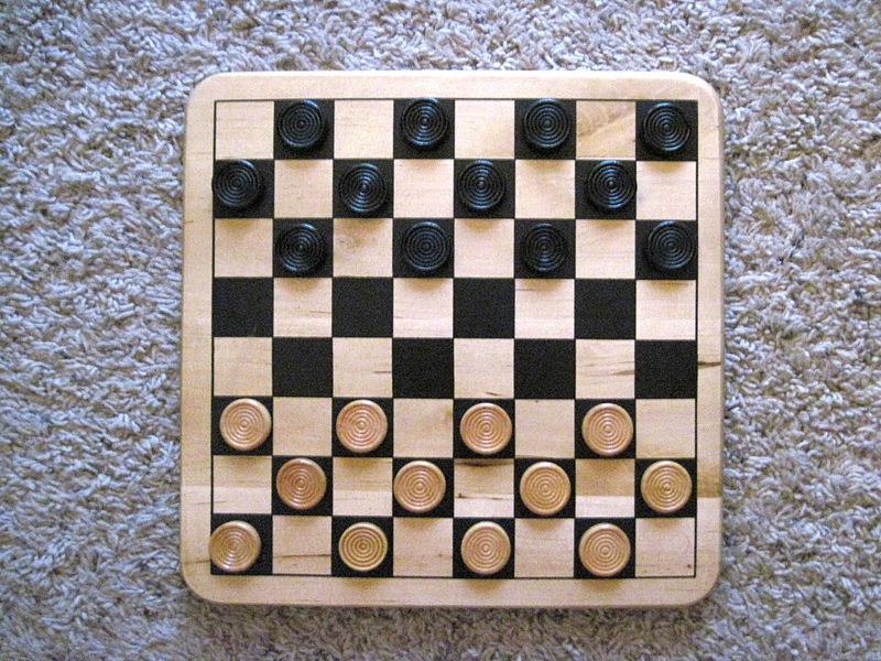 A wooden checkers board set up for a new game with black and light wooden pieces