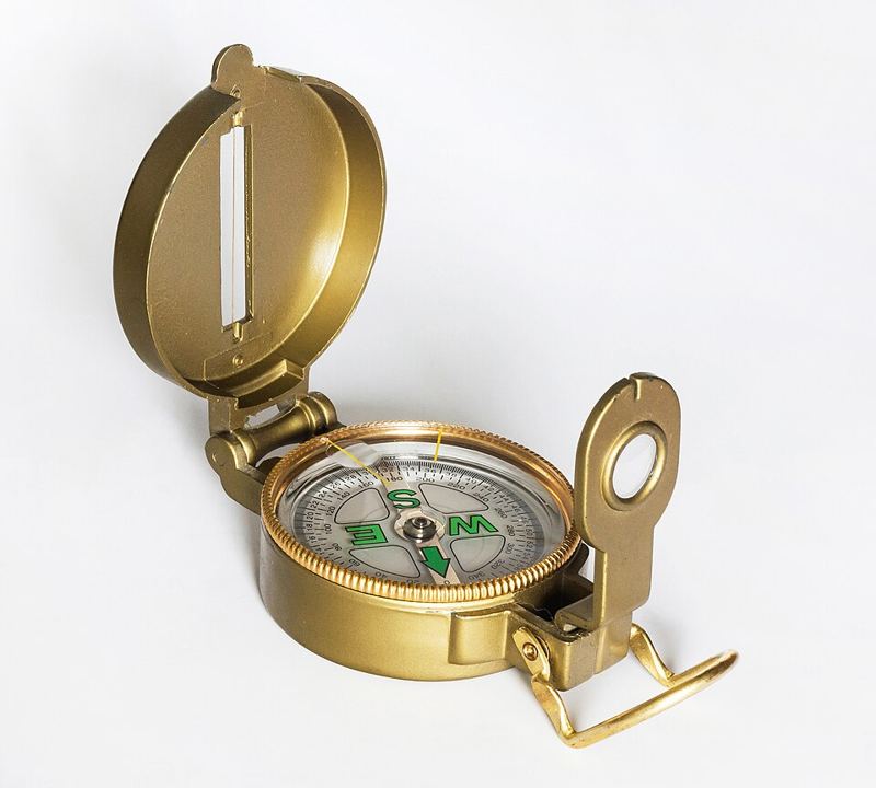 Brass lensatic compass with an open lid and sighting arm showing a magnetized needle dial