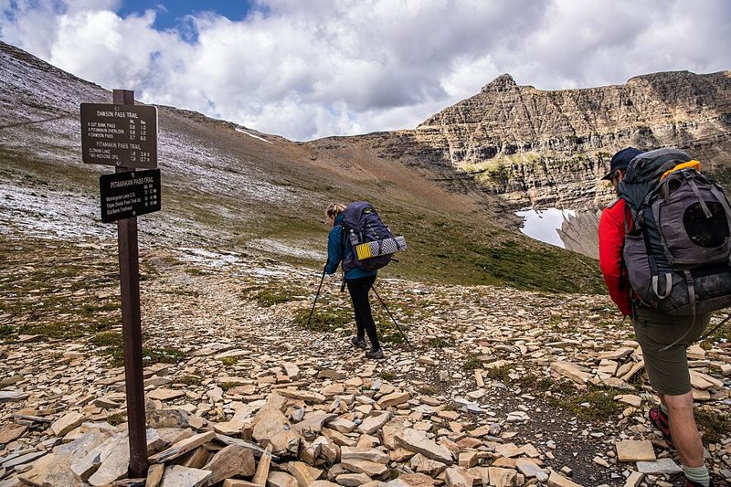Two backpackers carrying loaded packs on a rocky mountain trail in Glacier National Park