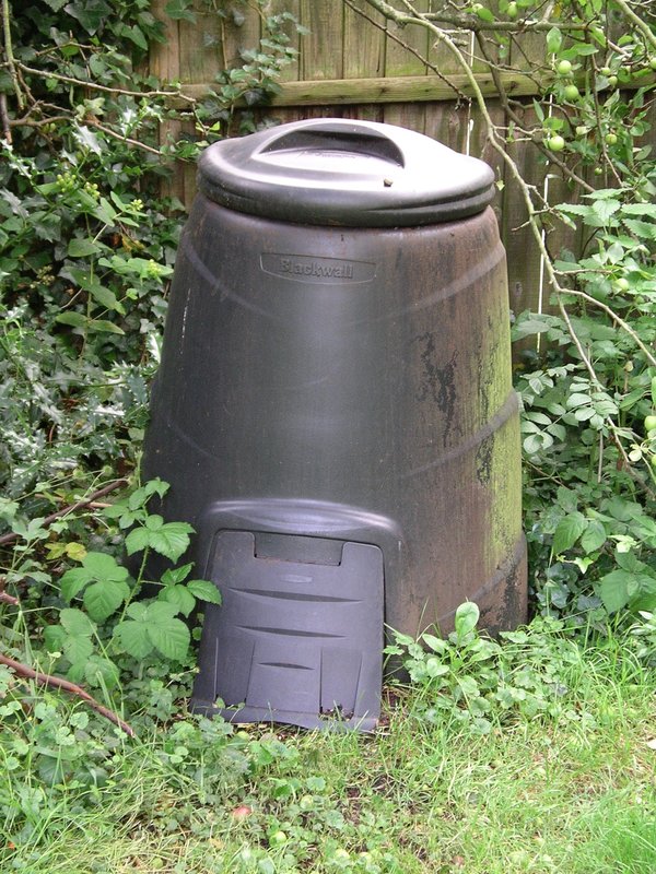 Black plastic backyard compost bin with a door at the bottom in a garden