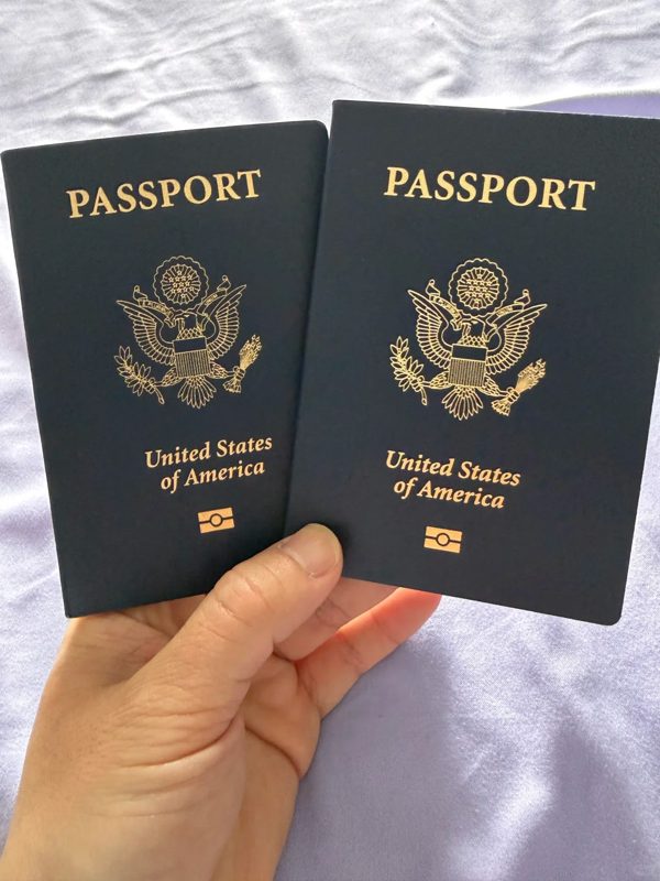 Hand holding two dark blue United States passport books, an older and a newer cover design