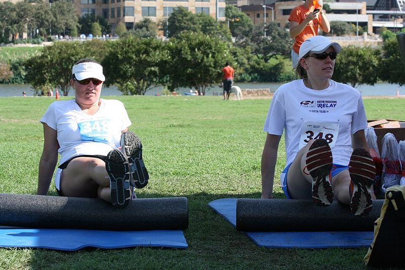 Two runners using foam rollers on their calves after a race