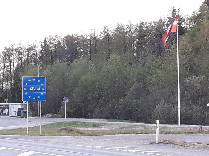 An EU-style blue border sign reading Latvija beside a Latvian flag at a Schengen internal border crossing