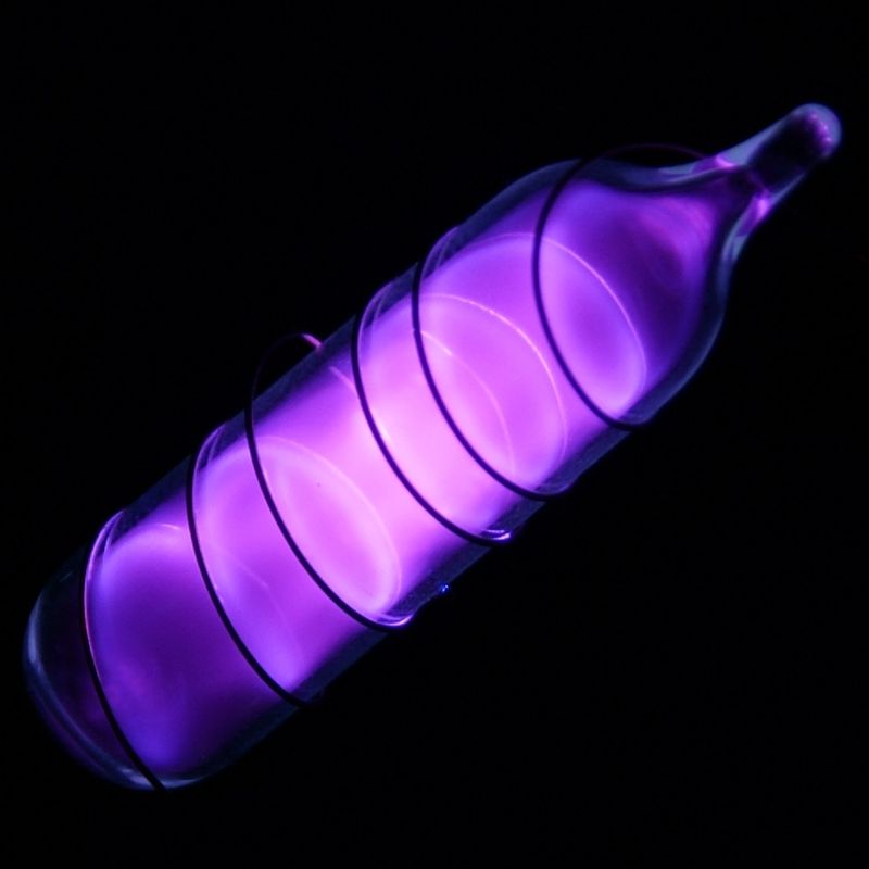A small glass vial of ultrapure argon gas glowing violet in the dark