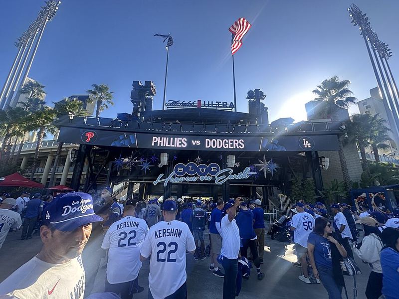 Fans in Dodgers jerseys walking toward a Dodger Stadium entrance under a Phillies vs Dodgers sign during the 2025 National League Division Series