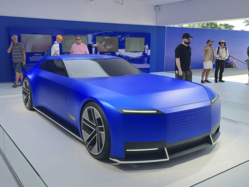 A blue Jaguar Type 00 electric concept car on display with visitors standing around it