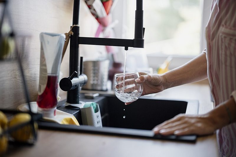 A person filling a glass with tap water at a kitchen sink