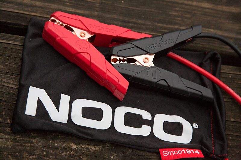 Red and black jumper cable clamps from a portable jump starter, used when learning how to jump start a car