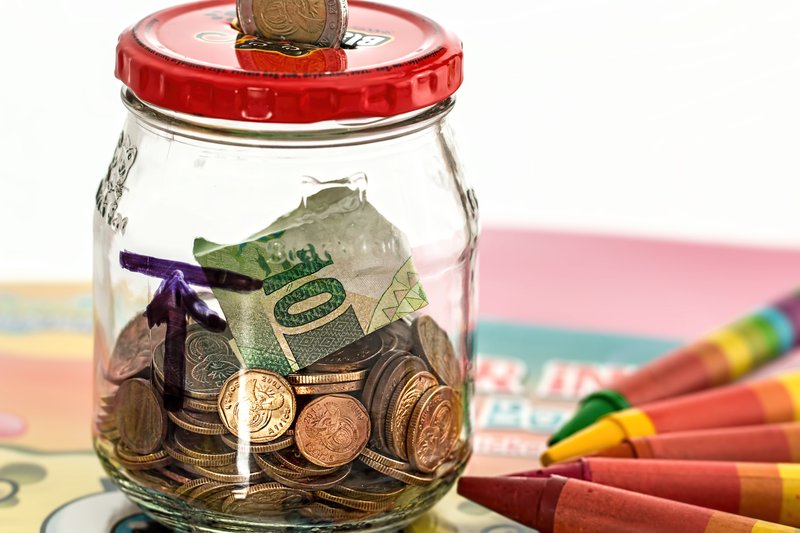 A glass jar piggy bank filled with coins used for savings