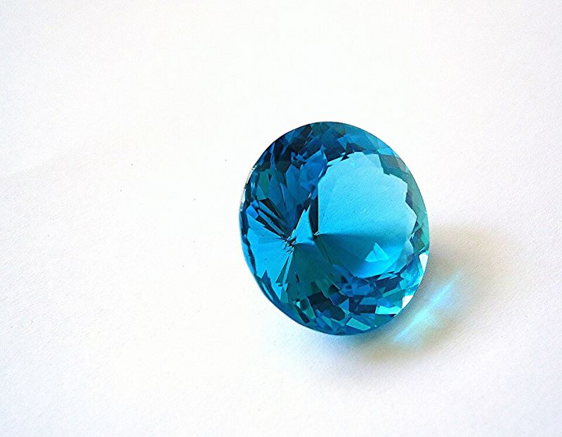 A round faceted bright blue topaz gemstone on a white surface