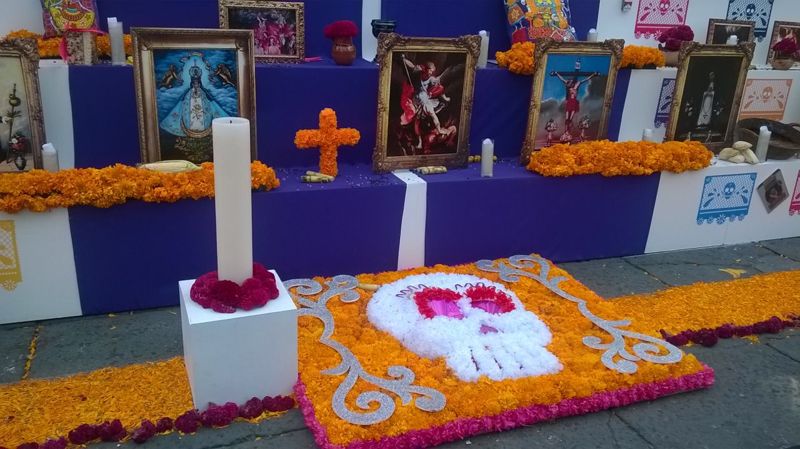 Day of the Dead ofrenda in Mexico City's Zócalo with marigolds, candles, a marigold cross, a flower skull and framed Catholic religious paintings