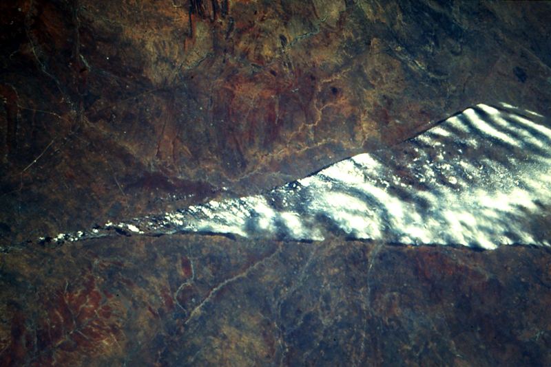A long band of white jet stream clouds crossing a brown landscape, photographed from orbit
