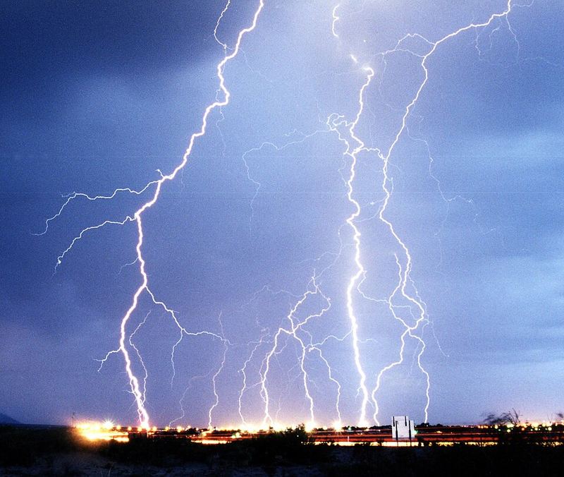 Multiple cloud-to-ground lightning bolts striking at night over a desert town