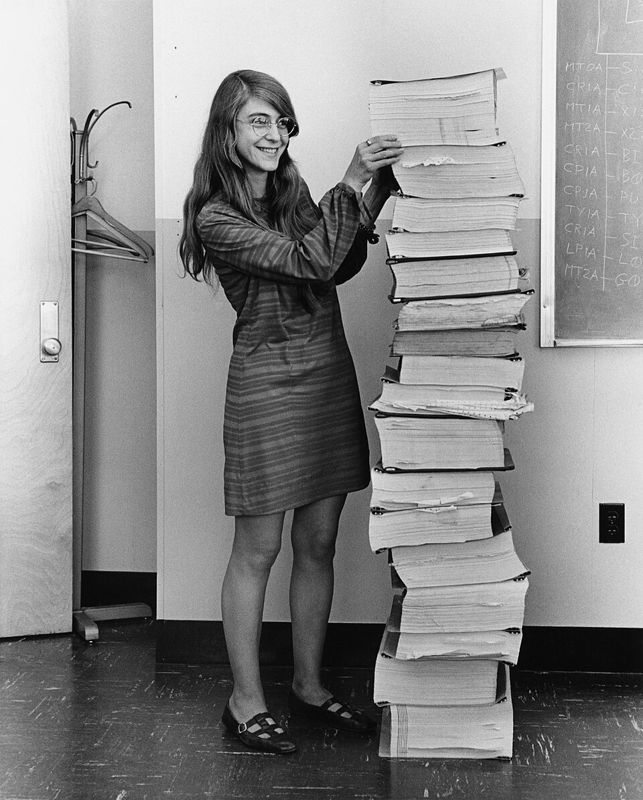Margaret Hamilton standing next to a tall stack of printed Apollo guidance software listings
