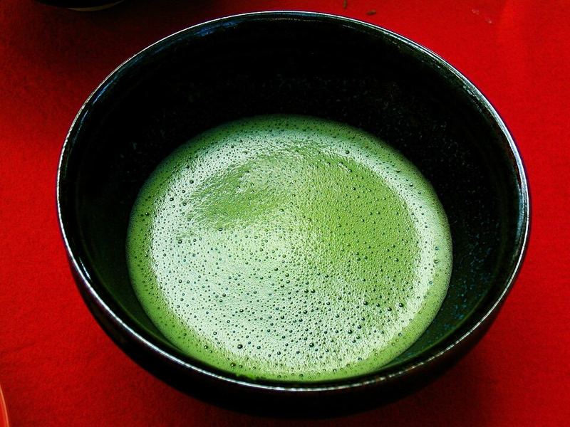 Whisked bright green matcha tea with fine foam in a dark ceramic bowl on a red cloth