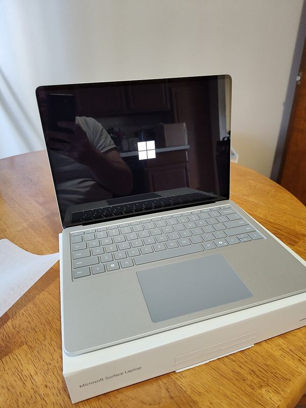 An open silver Microsoft Surface laptop sitting on its box on a wooden table