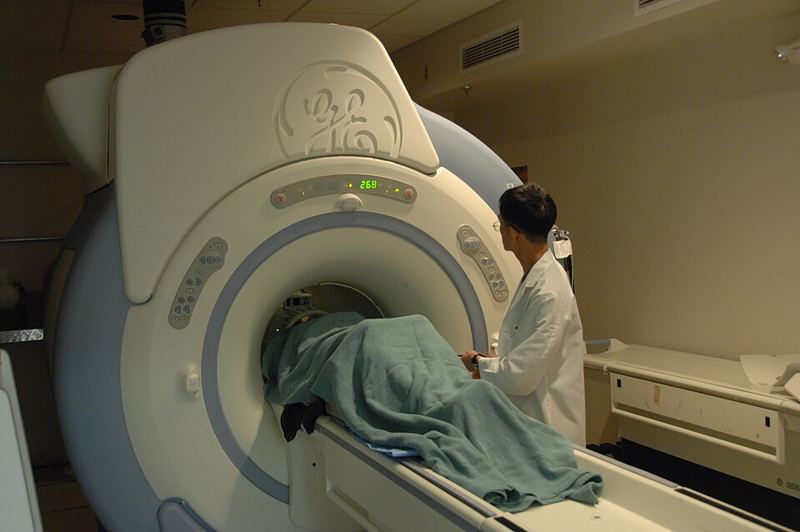 A technician in a white coat checks an MRI scanner as a patient lies inside under a blanket