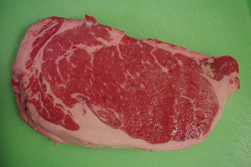 A raw marbled beef steak on a green cutting board