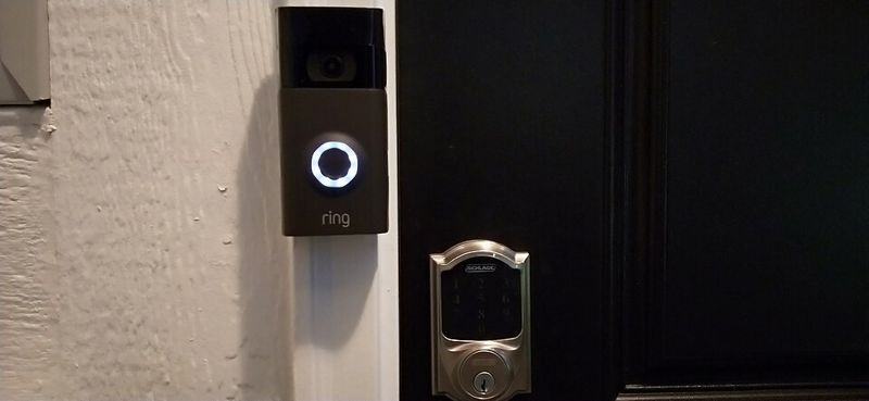 A Ring video doorbell mounted next to a front door with a keypad deadbolt lock