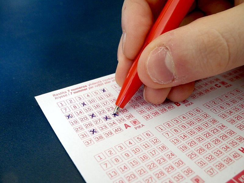 Hand marking numbers on a lottery ticket with a red pen