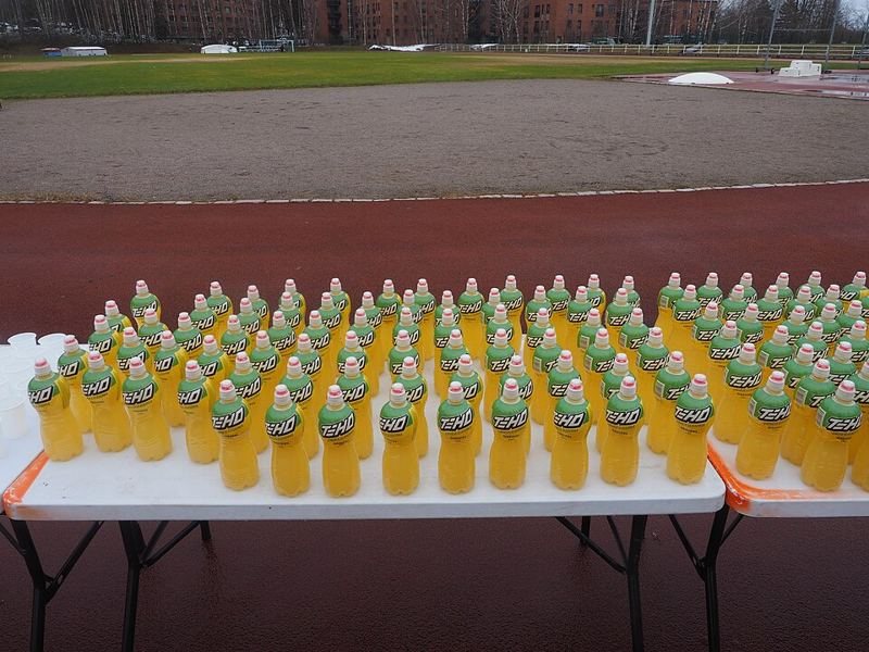 Rows of yellow sports drink bottles on a table beside a running track