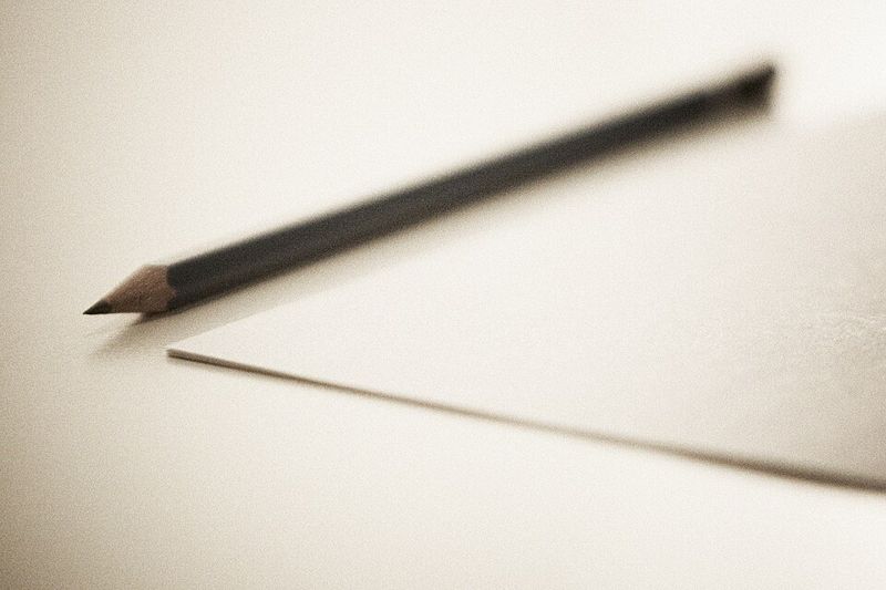A sharpened wooden graphite pencil lying next to a sheet of paper