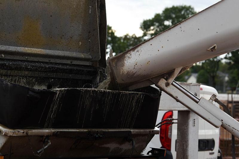 Wet concrete pouring from a truck chute into a concrete pump hopper at a construction site