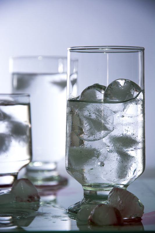 Glass of water with ice cubes, with more ice cubes melting on the table
