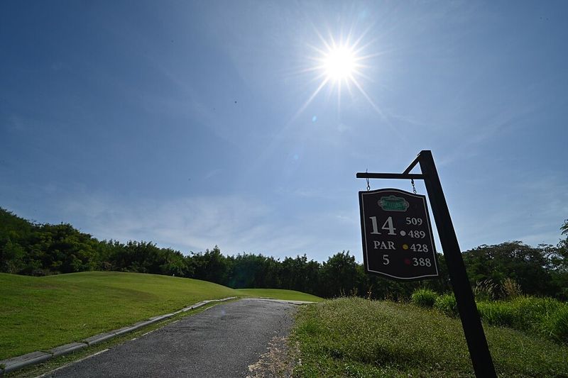 A par 5 hole sign for the 14th hole beside a cart path on a sunny golf course