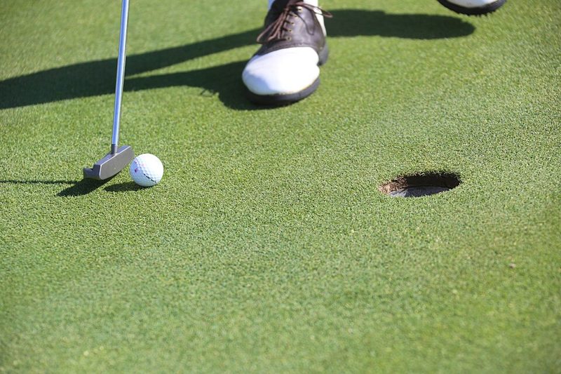 Golf ball next to a putter a few feet from the hole on a putting green