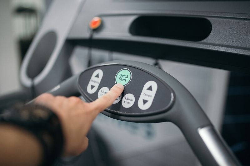 A hand pressing the Quick Start button on a treadmill console with incline and speed controls