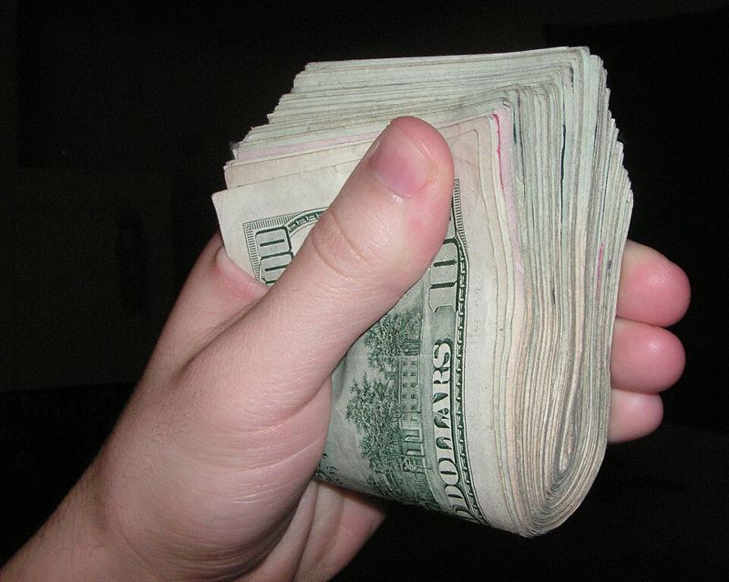 A hand holding a thick folded stack of US dollar bills