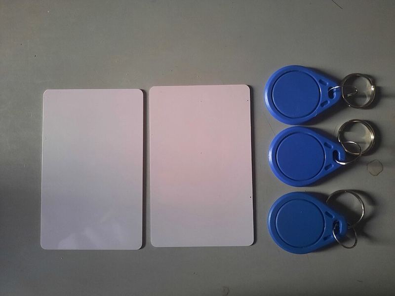 Two white 13.56 MHz RFID cards and three blue RFID key fobs on a gray table