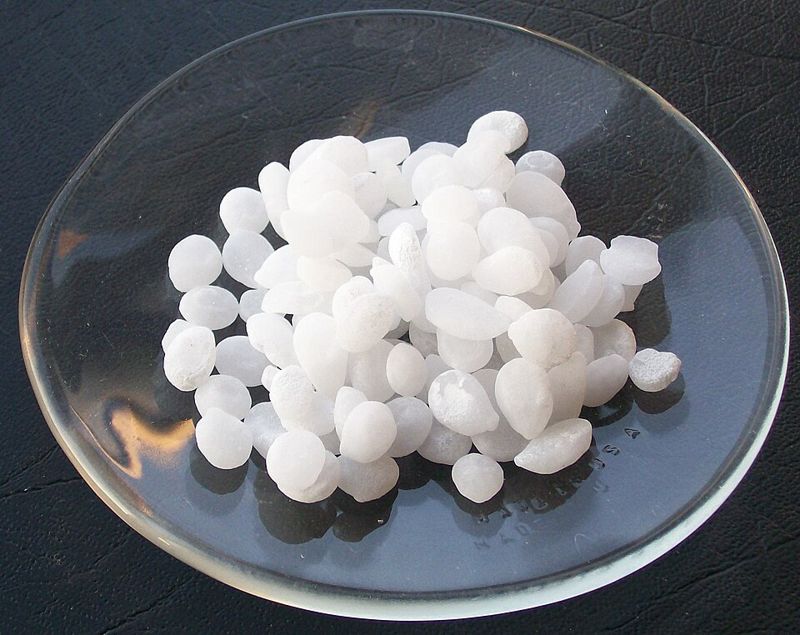 White pellets of sodium hydroxide, a strong base, in a glass dish